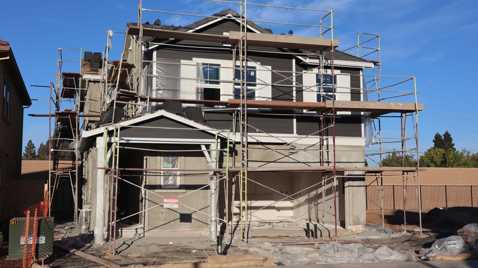 Two-story house inside scaffolding with gray siding going up