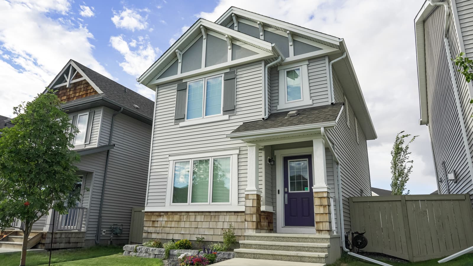 Two-story house with gray lap siding, shake gables and a stone base