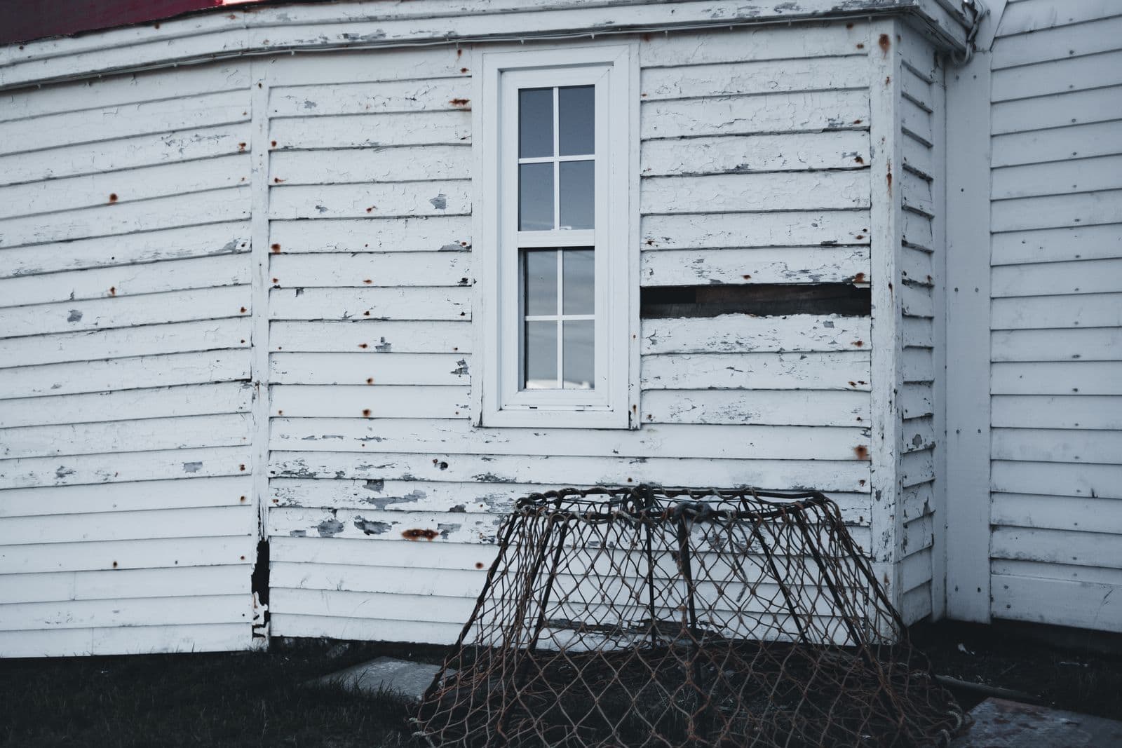 Weathered white lap siding with worn paint around a window